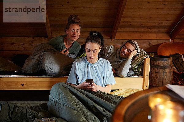 Freunde schauen Frauen an  die ein Smartphone benutzen  während sie sich auf einem Bett in einem Ferienhaus entspannen