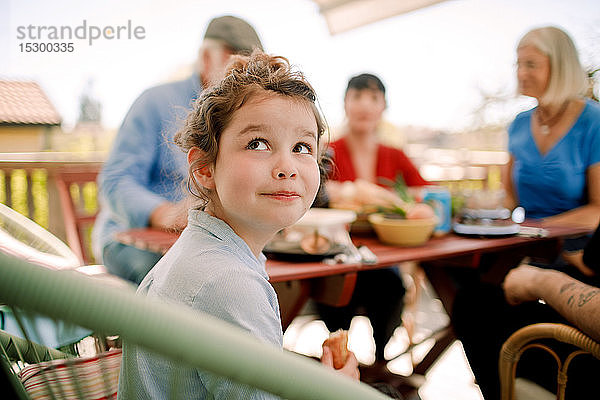 Lächelndes Mädchen schaut auf  während es mit der Familie am Tisch im Innenhof sitzt