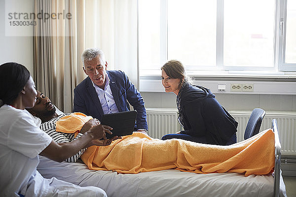 Ärztin zeigt digitales Tablett einem Patienten mit Familie auf der Krankenhausstation