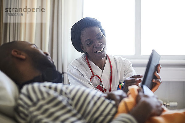 Lächelndes medizinisches Personal zeigt dem Patienten bei Routineuntersuchungen auf der Krankenstation ein digitales Tablett