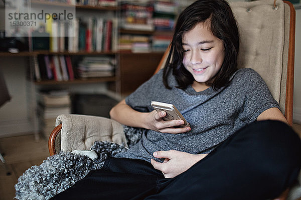 Lächelnder Junge nutzt soziale Medien auf einem Smartphone  während er zu Hause sitzt