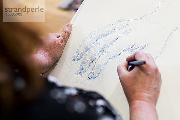Hochwinkel-Nahaufnahme einer Künstlerin  die eine menschliche Hand zeichnet.