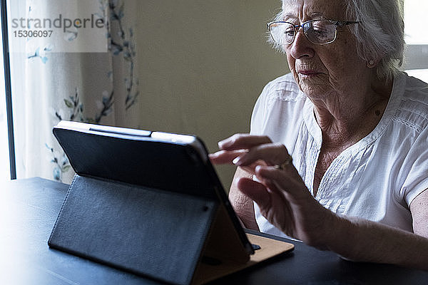 Nahaufnahme einer älteren Frau  die mit einem digitalen Tablett an einem Tisch sitzt und den Touchscreen benutzt.