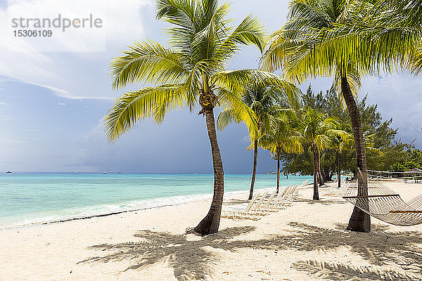 Ein weißer Sandstrand  türkisfarbenes Meer und Palmen.