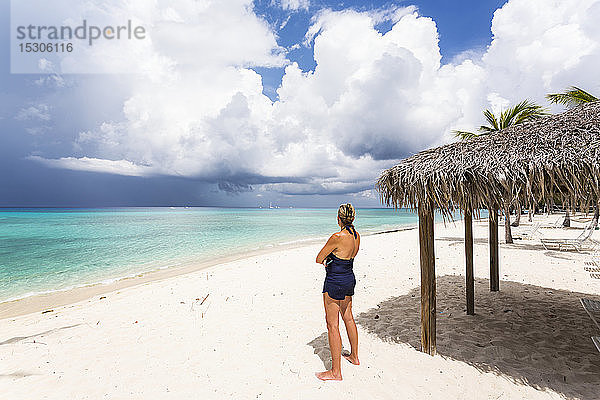 Erwachsene Frau beobachtet herannahende Gewitterwolken von einem Strand aus