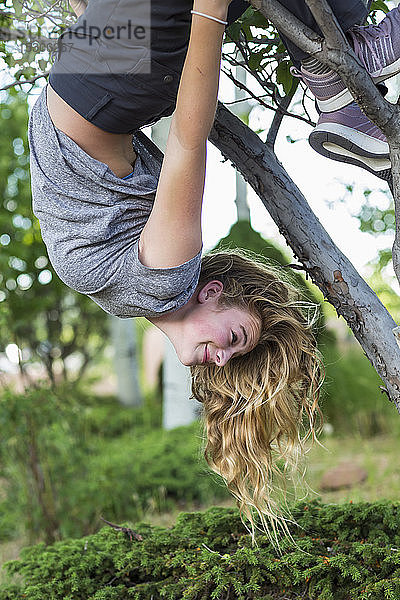 Ein Teenager-Mädchen hängt kopfüber vom Baum