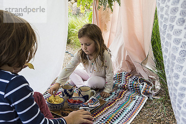 Junge und Mädchen spielen in einem improvisierten Zelt im Freien