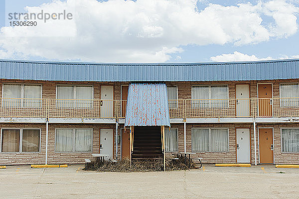 Verlassenes Motelgebäude mit einer rostigen Metallmarkise  zugezogenen Vorhängen an den Fenstern und Sturzkraut auf den Stufen.