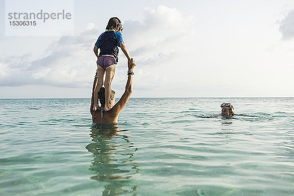 5-jähriger Sohn auf den Schultern der Mutter springt bei Sonnenuntergang in den Ozean