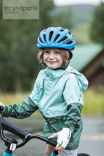 Porträt eines 5 Jahre alten Jungen in Regenjacke  der sich auf seinem Fahrrad abstützt
