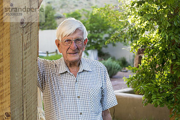 Ein älterer Mann steht auf einer Veranda vor seinem Haus.