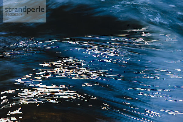Abstrakte Nahaufnahme von fließendem Flusswasser mit Lichtreflexionen an der Oberfläche.