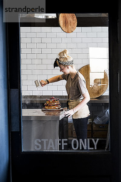 Blick durch eine Tür mit der Aufschrift Staff Only auf einen Koch  der in einer Großküche arbeitet und Puderzucker über einen Schichtkuchen mit frischem Obst streut.