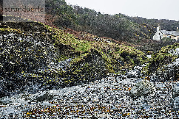 Das felsige Ufer von Pembrokeshire  eine Bucht mit einer Hütte am Wasser und Stufen zum Kiesstrand.