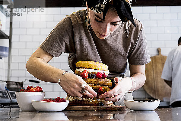Ein Koch  der in einer Großküche arbeitet und einen Biskuitkuchen mit frischen Früchten zusammensetzt.