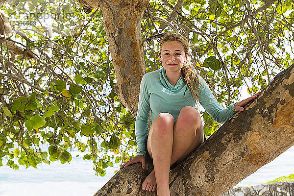 Ein jugendliches Mädchen sitzt lachend in einem Baum.