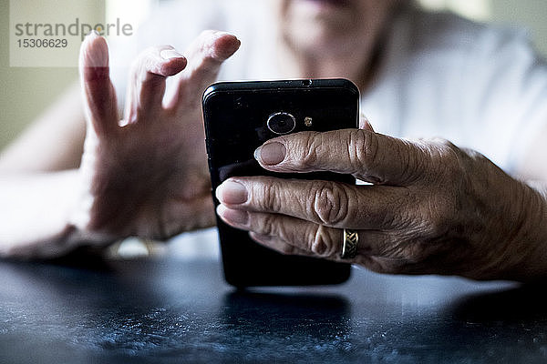 Nahaufnahme einer älteren Frau  die an einem Tisch sitzt und ein Mobiltelefon benutzt.