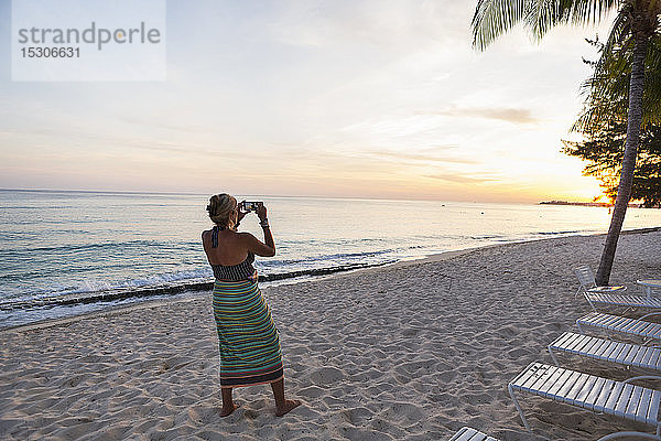 Erwachsene Frau fotografiert mit einem Smartphone am Strand