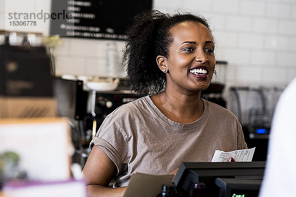 Eine Barista-Frau lächelt bei der Begrüßung neben dem Tresen in einem Café.