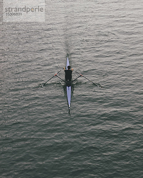 Draufsicht auf einen Ruderer in einem Boot mit nur einem Schädel auf ruhigem Wasser mitten im Schlag  Bewegungsunschärfe.