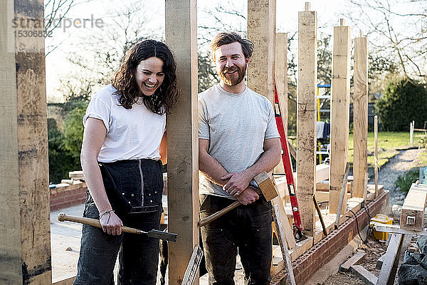 Lächelnder Mann und Frauen mit Handwerkzeugen in der Hand stehen auf der Baustelle eines Wohnhauses.
