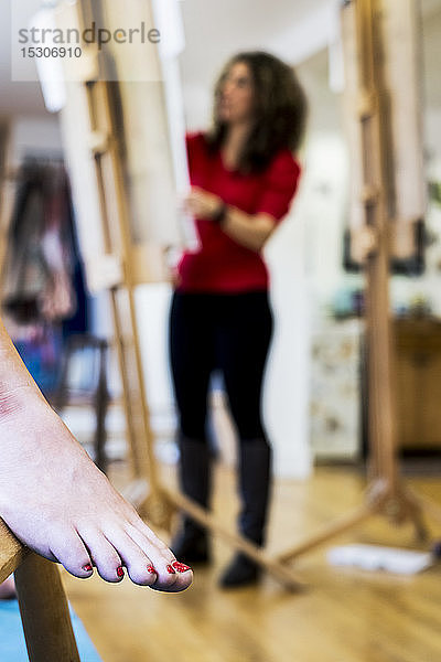 Nahaufnahme eines nackten weiblichen Fußes mit rot lackierten Zehennägeln  ein Modell in einem Zeichenkurs an der Kunstschule. Im Hintergrund arbeitet ein Künstler.