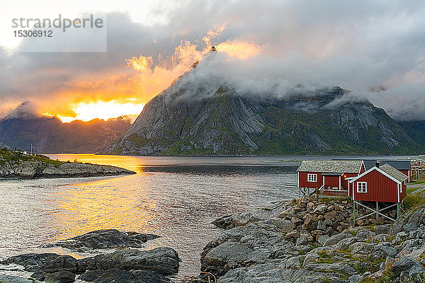 Niedrige Wolken wirbeln herum und bedecken die Berge  ein kleines traditionelles Rorbu-Haus an der Küste. Lofoten-Inseln