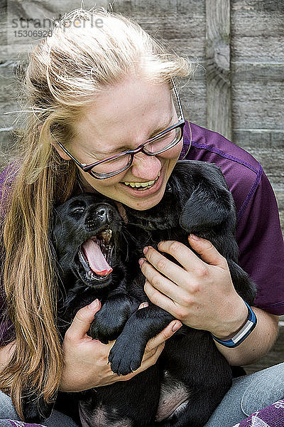 Blonde Brillenträgerin umarmt zwei schwarze Labrador-Welpen.