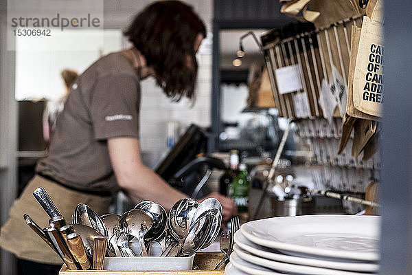 Nahaufnahme eines Stapels von Tellern und Behältern mit Besteck in einem Restaurant  Frau arbeitet im Hintergrund.