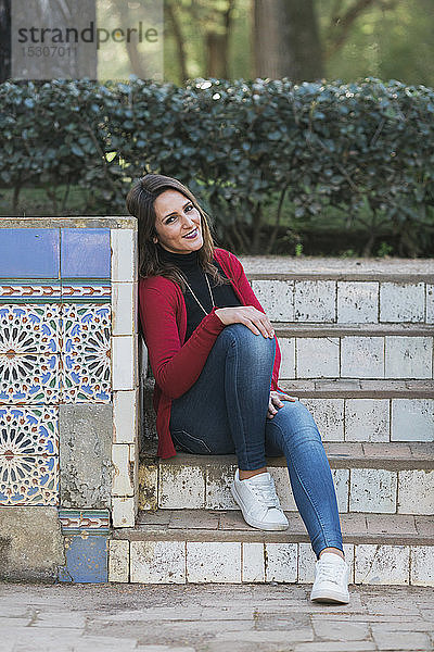 Porträt einer glücklichen Frau  die auf Parkstufen neben einer Mosaikwand sitzt