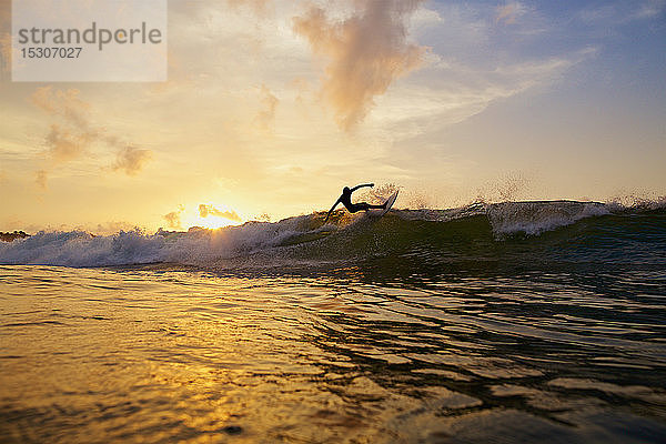 Männlicher Surfer  der bei Sonnenuntergang auf dem Meer eine Kurve von der Welle macht  Sayulita  Nayarit  Mexiko