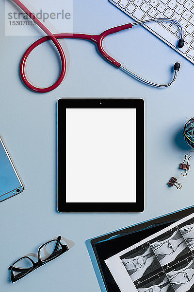Ansicht eines Formulars über einem digitalen Tablet  umgeben von Röntgenbildern und einem Stethoskop auf dem Schreibtisch