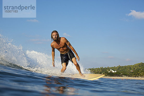 Männlicher Surfer reitet auf einer sonnigen Meereswelle