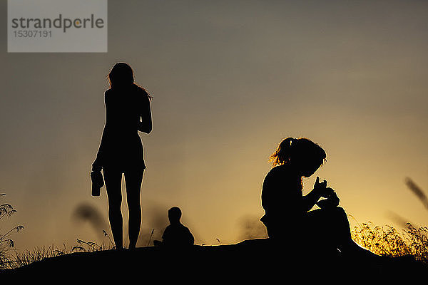 Silhouette Frauen essen und trinken auf einem Hügel bei Sonnenuntergang