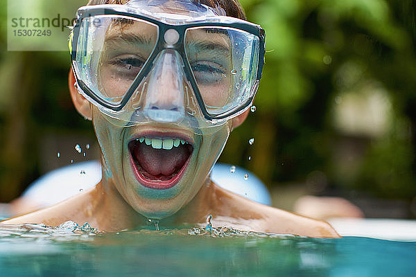 Porträt übermütiger Junge mit Schwimmbrille beim Schwimmen