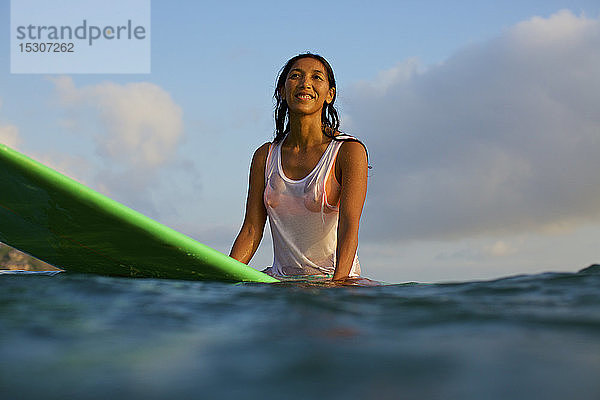 Lächelnde  selbstbewusste weibliche Surferin wartet auf dem Surfbrett im Meer