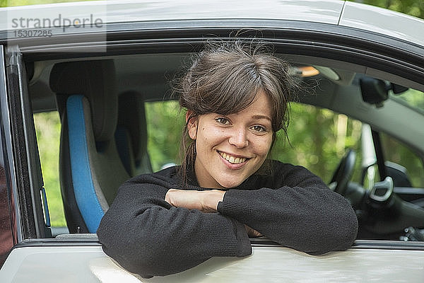 Porträt einer lächelnden jungen Frau  die sich aus dem Autofenster lehnt