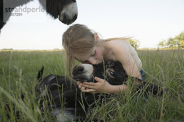 Mädchen umarmt und küsst Baby Esel im Gras