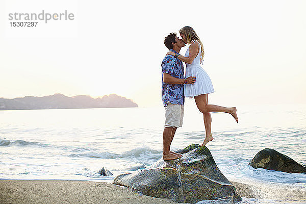 Zärtliches  romantisches junges Paar  das sich auf einem Felsen am Meer küsst  Sayulita  Nayarit  Mexiko