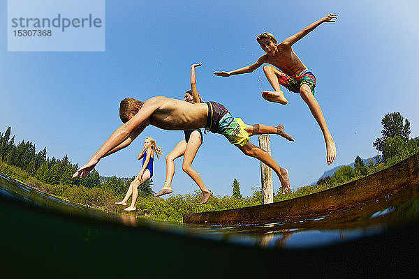 Verspielte Kinder springen vom Steg in den sonnigen Sommersee