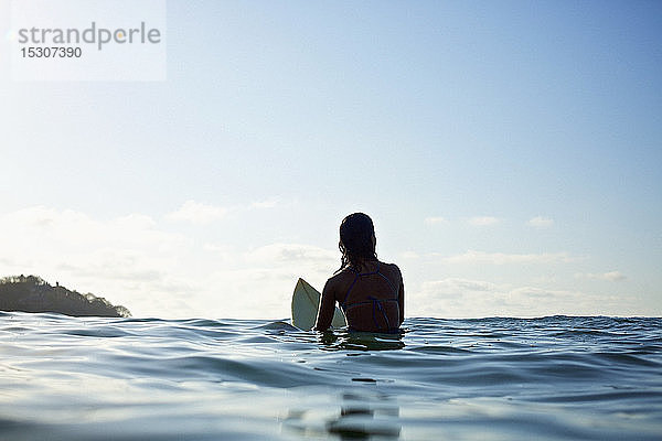 Silhouette einer weiblichen Surferin auf einem Surfbrett  die im sonnigen blauen Ozean wartet