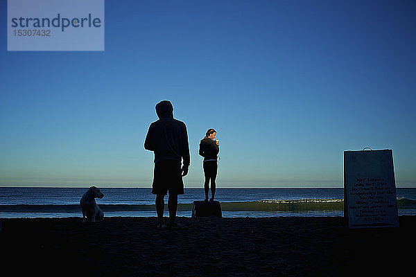 Silhouette junges Paar mit Hund am Strand bei Sonnenaufgang