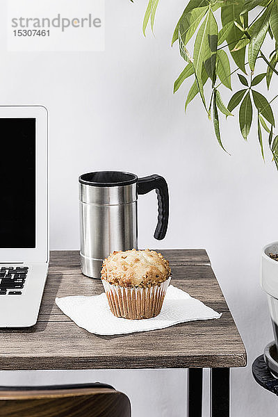 Isolierter Kaffeebecher und Muffin auf dem Schreibtisch neben dem Laptop im Büro