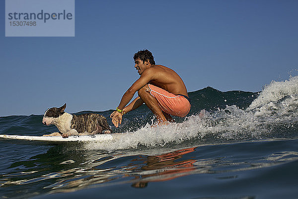 Junger Mann und Hund auf dem Surfbrett auf einer Meereswelle