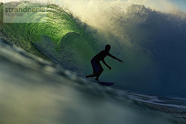 Silhouette eines männlichen Surfers auf einer beleuchteten Meereswelle