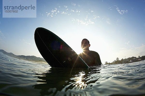 Silhouette männlicher Surfer auf dem Surfbrett im sonnigen Ozean