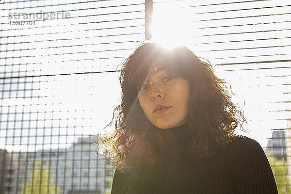 Porträt selbstbewusste junge Frau am sonnigen Zaun