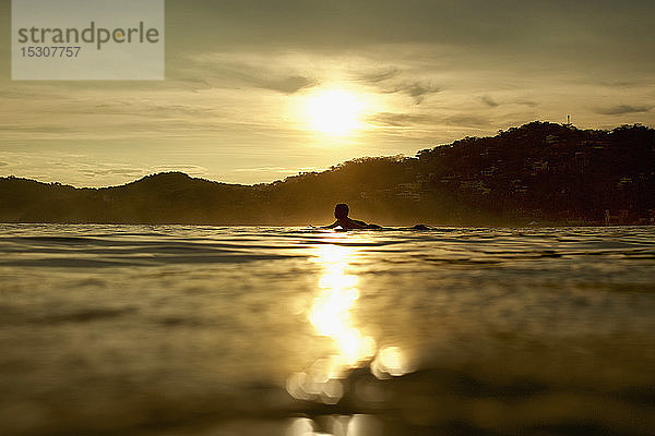 Silhouette eines jungen Mannes auf einem Surfbrett auf dem ruhigen Meer bei Sonnenuntergang  Sayulita  Nayarit  Mexiko