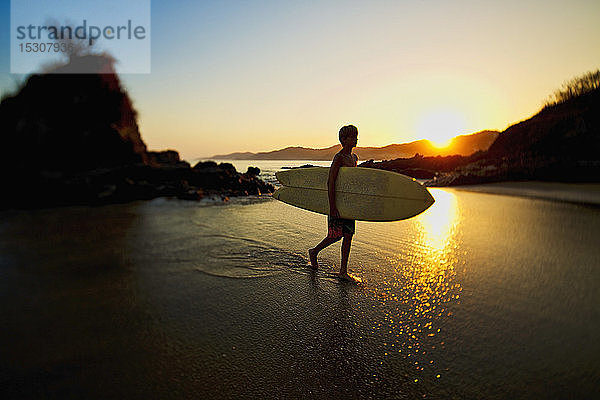 Silhouette eines Jungen mit Surfbrett an einem idyllischen Strand  Sayulita  Nayarit  Mexiko