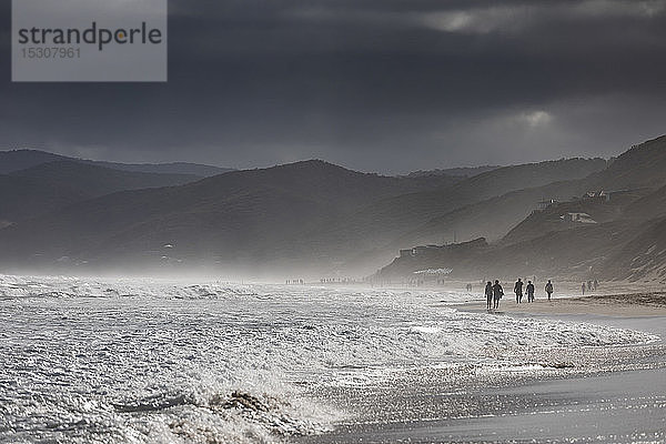 Bedrohliche Wolken über silhouettierten Menschen  die am Strand spazieren gehen  Aireys Inlet  Victoria  Australien